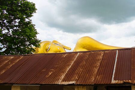 Face of Reclining Buddha behind zinc roof in Buddhist Temple, Ratchaburi Thailandの写真素材