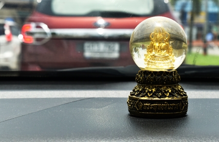 little buddha statue behind windshield in car ,text in thai language is Phraphutthachinnarachの写真素材