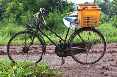old bicycle and orange basket on soil and mud road in countryside in morning after raining in last nightの写真素材
