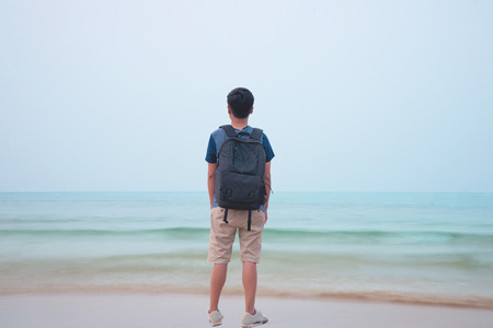 Young traveler  with backpack staying alone at seaside and looking to the ocean, exploring the world...