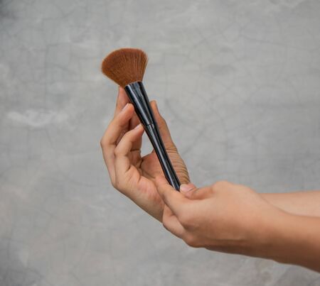 Close up hand cute girl with make up brush on grey background.