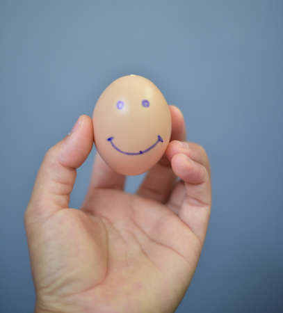 Egg smile sign in hand on gray background.