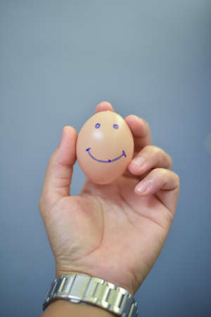 Egg smile sign in hand on gray background.の写真素材