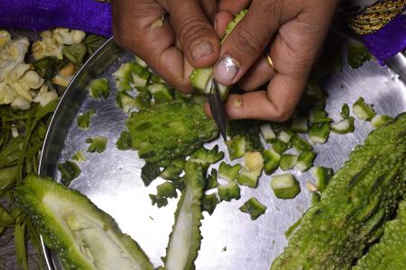 A woman,s hand and pieces of bitter gourd cutting bitter gourd with a knife