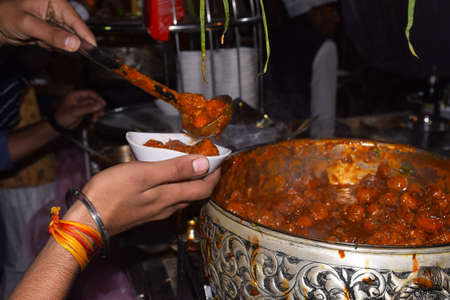 Hand of Indian man carrying Manchurian in his plate by a spoon from a large pot