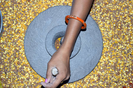 A village woman's hand, grinds gram in an old hand operated flour mill.