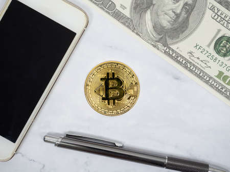 Gold bitcoin with phone and dollar and pen top viewの写真素材