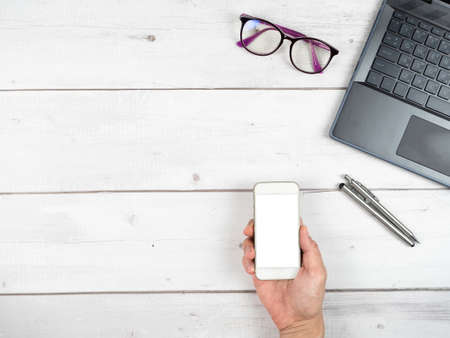 Laptop glasses coffee cup and two silver pen office workspace top view and hand hold smartphone white screen copy spaceの写真素材