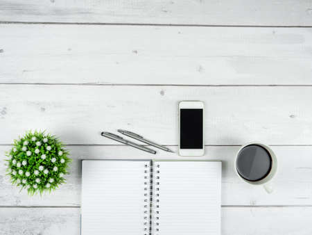 Office workspace top view copy space ,Smartphone black screen on black page notebook with glasses and two silver pen on white wood tableの写真素材