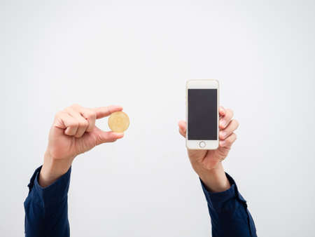 Closeup hand holding golden bitcoin coin and mobile phone in hand on white isolated backgroundの写真素材