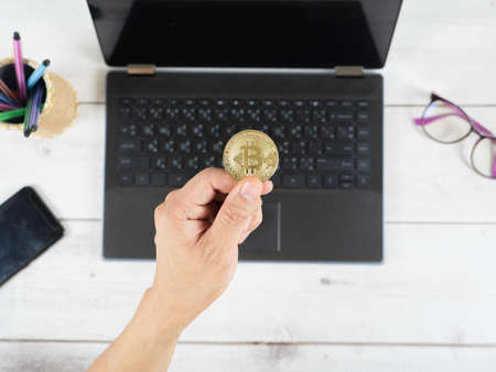 Hand holding bitcoin on the keyboard of laptop background on table top view workspaceの写真素材