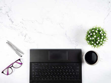 Keypad laptop with glasses silver pen coffee cup flower vase on marble table workplace copy space top viewの写真素材