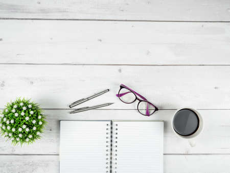 Office workspace top view copy space ,Smartphone black screen on black page notebook with glasses and two silver pen on white wood tableの写真素材