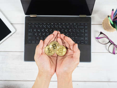 Hand holding gold bitcoins on the keyboard of laptop background on table top view workspaceの写真素材