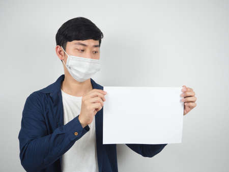 Asian man with mask protect looking at blank paper in his hand on white backgroundの写真素材
