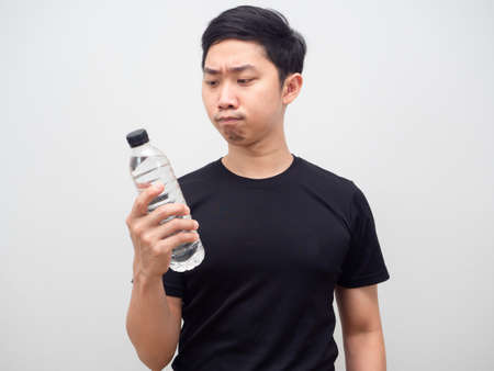 Asian man looking at water bottle in his hand and feeling hesitage on white backgroundの写真素材