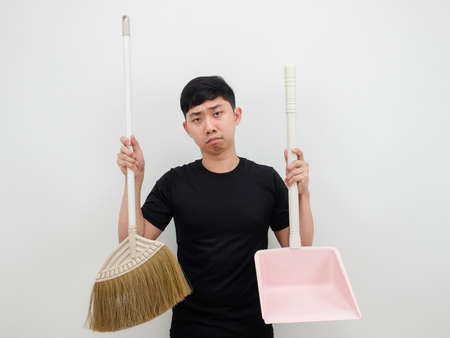 Asian man holding dustpan and broom feeling bored to clean house on white backgroundの写真素材