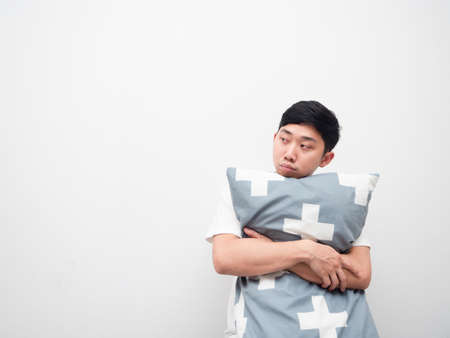 Asian man hug pillow feeling sleepy look at space white backgroundの写真素材