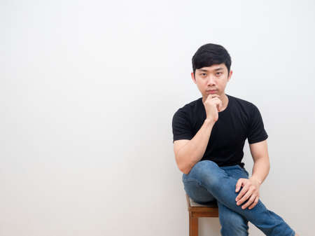 Asian man sitting on chair with confident face looking at camera on white backgroundの写真素材