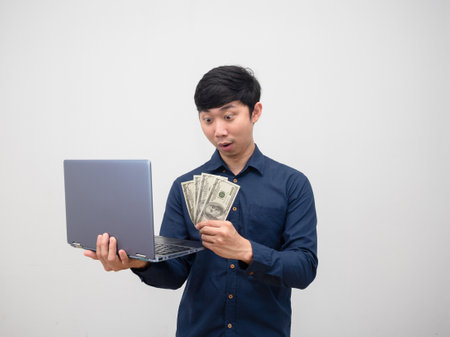 Asian man look money in his hand and holding laptop feeling amazed on white background