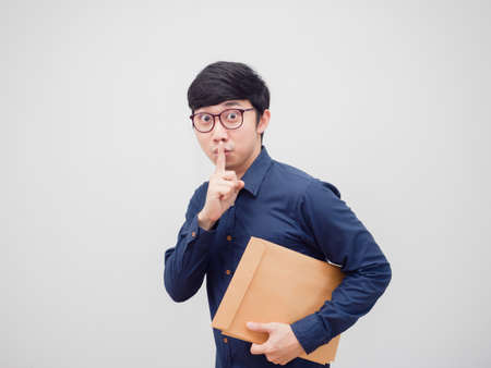 Asian man wearing glasses holding document envelope hand shh escape from work concept white backgroundの写真素材
