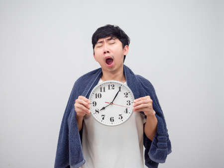 Sleepy man yawn show clock in his hand and cover body by towel on white background