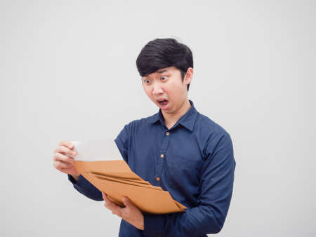 Asian man holding document envelope and reading the paper in hand feeling shocked white backgroundの写真素材