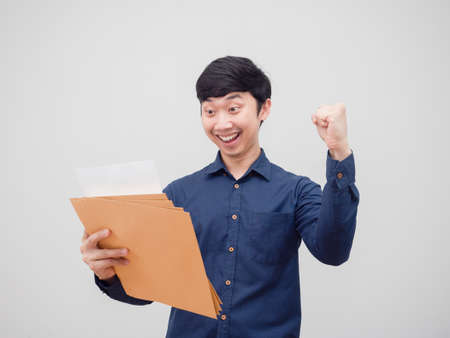 Asian man reading at document envelope in hand feeling happy and smile show fist up white backgroundの写真素材
