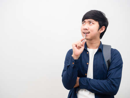 Asian man with backpack bite pen serious face thinking something look at space white backgroundの写真素材