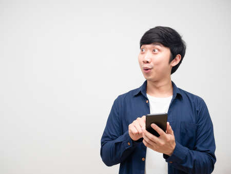 Asian young man holding and press mobile phone in his hand feeling excited and lookign at copy space white isolatedの写真素材