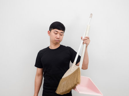 Asian man holding dustpan and broom feeling bored to clean house on white backgroundの写真素材