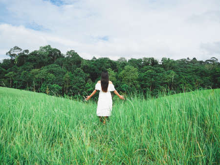 Traveler girl in white dress stand in meadow and forest and mountain with sky and cloudy background landscape,Woman in grass field with sky and tree and cloudy at vacationの写真素材