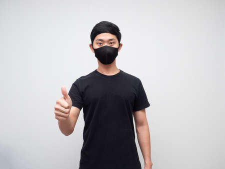 Asian man wearing protect mask show thumb up looking at camera white backgroundの写真素材