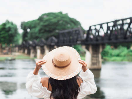 Asian woman with hat and River Kwai Bridge historic place background in Kanchaburi Thailandの写真素材
