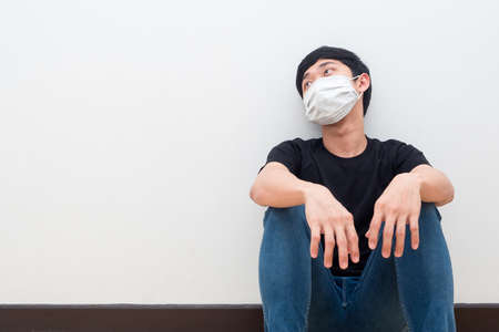 Drepressed man wearing protect mask sit against the wall sad emotionの写真素材