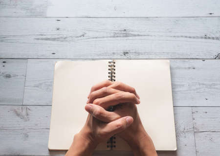 Praying hands on book blank page and sunlight nature shadow on white wooden texture background top view,Pray god conceptの写真素材