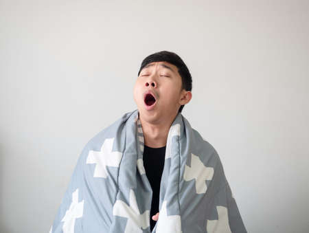 Man wake up with blanket cover his body and feel sleepy and yawn close the eye on white isolatedの写真素材