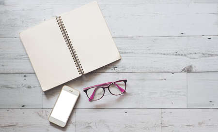 Open notebook blank page with smartphone and glasses on white wood table nature shadow and light top view space,Business conceptの写真素材