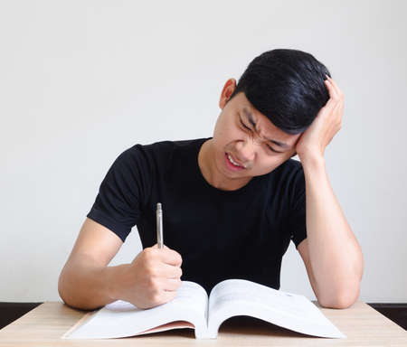 Young man with pen serious and feel strain with problem touch his head by hand with the book on the...