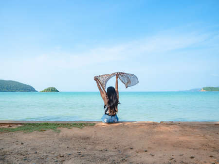 Woman sit at the beach show scarf up with blue ocean blue sky and mountain landscape bright sunlight,Holiday at the beautiful beach conceptの写真素材