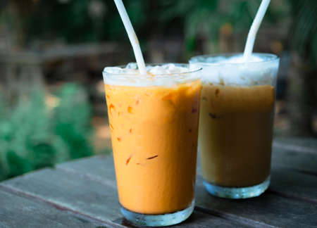 Closeup Thai tea and coffee ice milk white on wood table in cafe and tree backgroundの写真素材