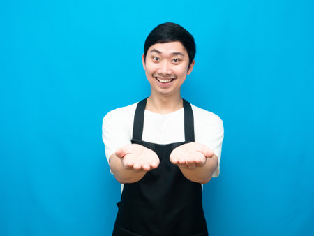 Man apron showing empty hand uo with happy smile blue backgroundの写真素材