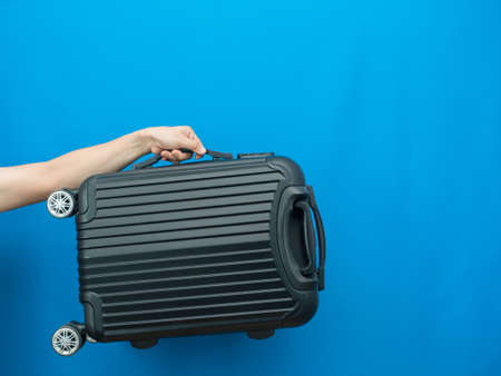 Man hand holding luggage on blue background holiday concept