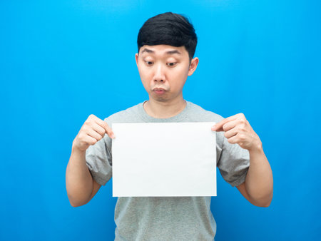 Asian man gesture doubt looking at blank sheet in hand blue backgroundの写真素材