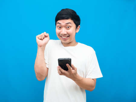 Man holding cellphone gesture happy show fist up blue backgroundの写真素材