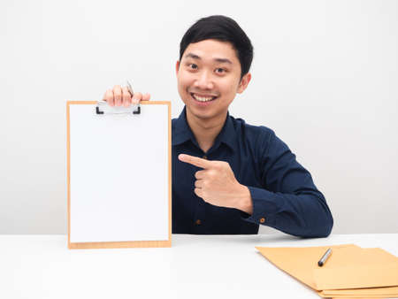 Handsome man smile face sitting at the table and point finger at blank paper on woodboard white...