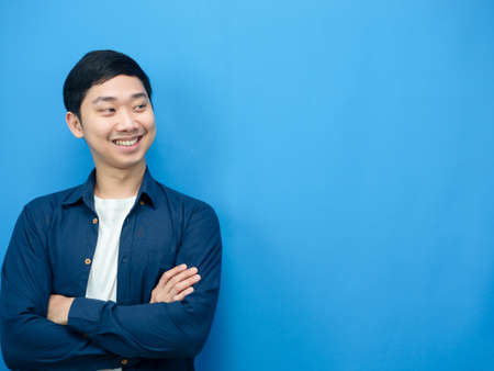 Asian man smile and cross arm looking at copy space blue backgroundの写真素材