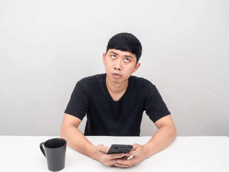 Man holding mobile phone at table feeling bored looking upの写真素材
