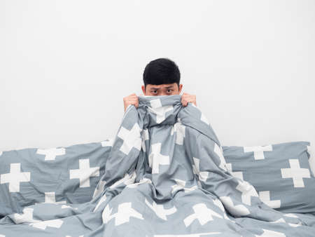 Man on the bed cover blanket his body and face feeling afraidの写真素材