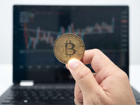 Hand holding bitcoin front of laptop crypto grapb in screen,Digital money economy